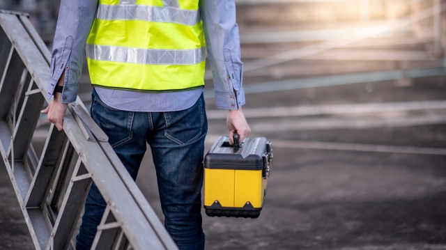 A worker carrying a platform ladder for a repair job.