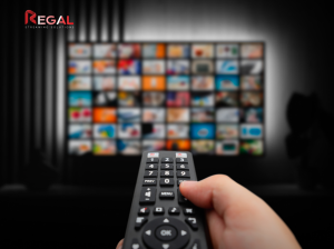 Close-up of a hand holding a remote control, pointing at a TV screen displaying a grid of streaming content, with the Regal Streaming Solutions logo in the top left corner.