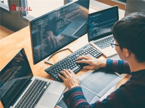 Developer working on multiple screens with programming code displayed, surrounded by laptops and monitors, with the Regal Streaming Solutions logo in the top-left corner.