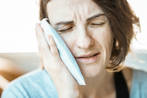 A woman holding a cold compress against her cheek to relieve a toothache.