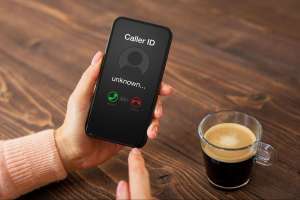A person holding a smartphone showing an incoming call from an unknown number, representing the can you hear me phone scam.