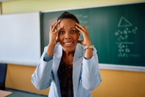 Frustrated black teacher holding her head in pain and looking at camera.