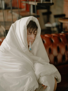 A man looks sick while wearing a blanket.