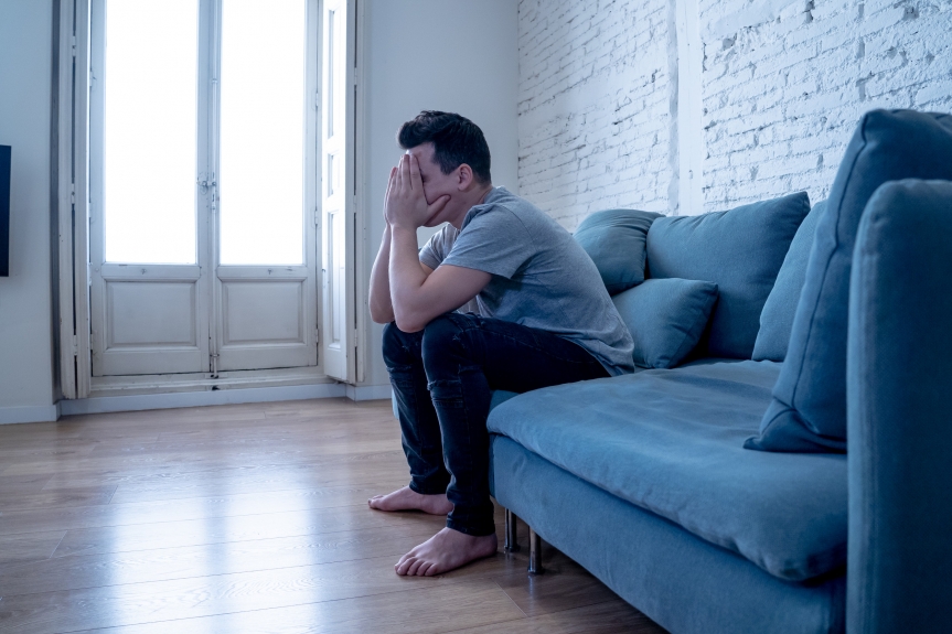 young man sitting on couch stressed over home problems